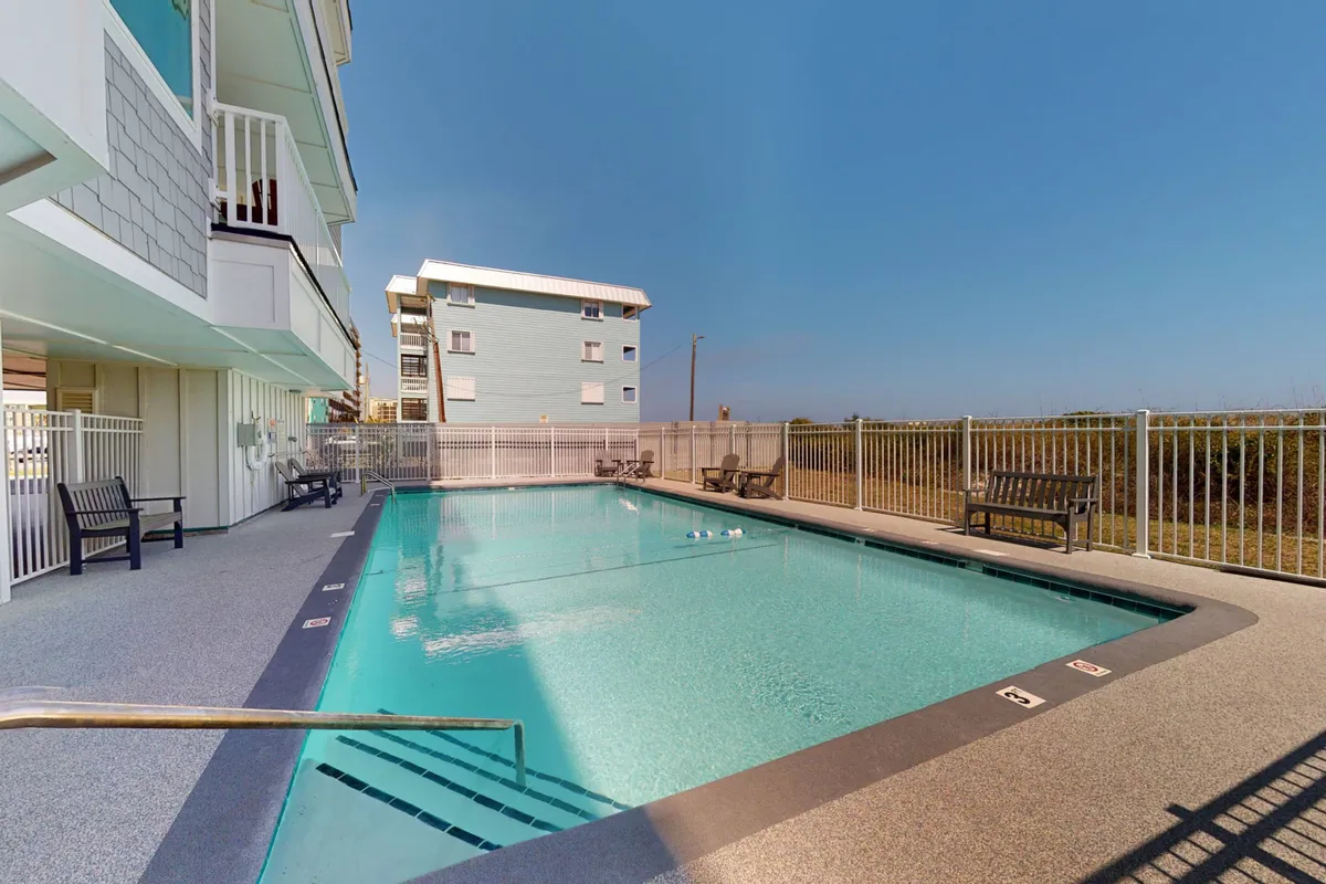 A sparkling outdoor pool surrounded by benches and set under a blue sky, inviting guests for a swim or sunbathing. The scene evokes the feel of a resort-style amenity right at home.
