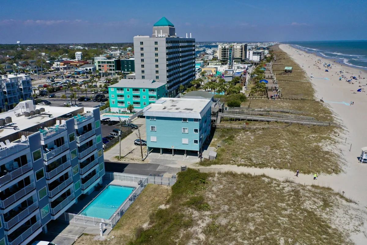 This exterior image captures the beachfront community with the ocean, pool, buildings, and boardwalk all visible. People are seen enjoying various activities like swimming, sunbathing, beach walking, and dining outdoors. The vibrant and relaxed atmosphere is underscored by the golden light, emphasizing both beach access and luxurious leisure.