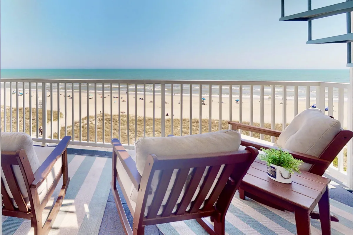This image features a rooftop or balcony setting with comfortable outdoor seating, a small table with a plant, and an expansive ocean view. The tranquil vibe and elevated perspective suggest a private space perfect for unwinding and enjoying the scenery.