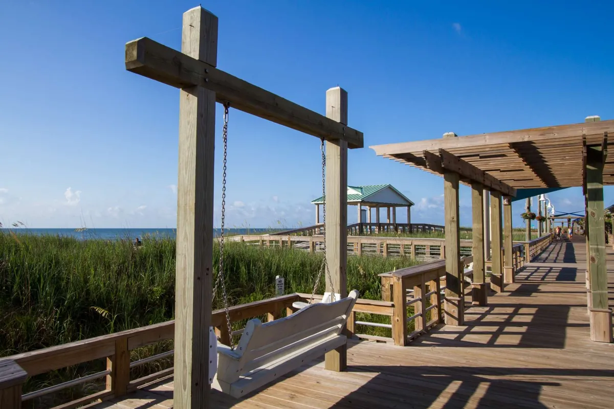 This image captures a picturesque swing on the boardwalk overlooking the ocean, with a gazebo nearby and sweeping views of the water and sky. The natural scenery is inviting, and the boardwalk setting hints at a communal spot for gatherings or leisurely strolls.