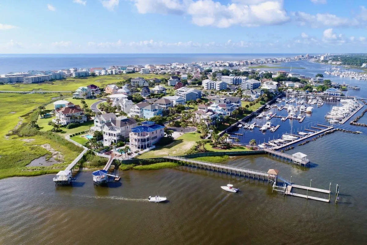 A sweeping view over coastal homes, the marina, boats, and green fields conveys the broader context of the Carolina Beach community. The relaxed mood suggests opportunities for boating, fishing, and exploring local events, capturing the essence of the destination's vibrant and scenic lifestyle.